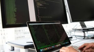 Core DevOps Skills: Developer coding on laptop with dual monitors.