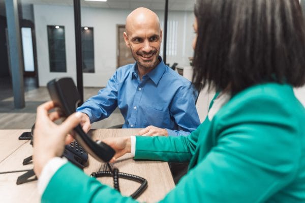 Customer service representative hands phone to smiling customer. Office setting.