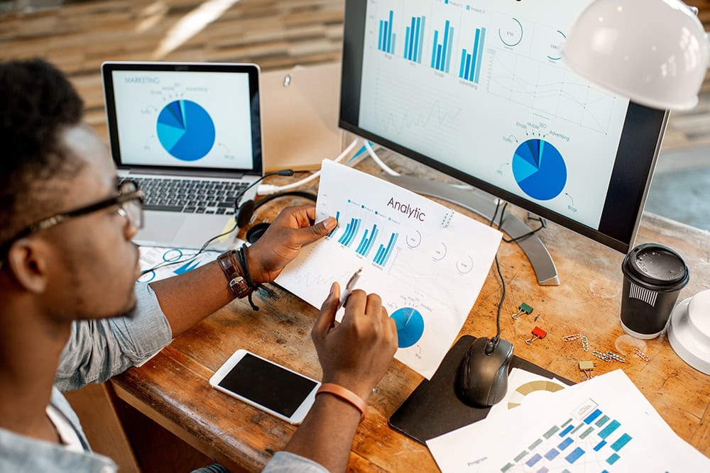 Data Analytics Specialist reviewing charts. Graphs on screen, data analysis in progress.