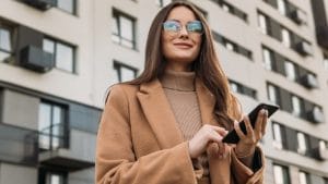 Adult matric English home language banner: Woman with phone, wearing coat and glasses.