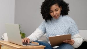 Woman studying online for Business Management Short Course. Laptop and clipboard on a desk.