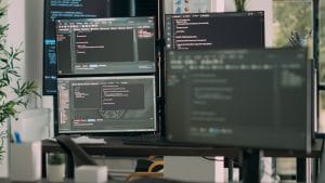 Network engineer's desk with multiple monitors displaying code. CloudOps, network security, and software development.