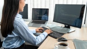 SecOps Engineer working at computer. Penetration Tester coding on multiple monitors. Cybersecurity professional.