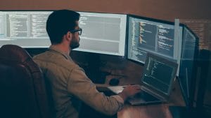 Programmer working on API development. Developer coding on multiple monitors.