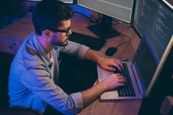 Agile programmer securing code. Man coding on laptop with multiple monitors. Software developer at work.