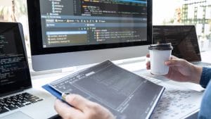 Software Project Analyst to Manager: Coder with laptop, coffee, and code on screen.