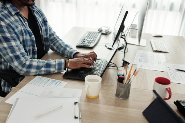 Technical bundle. Person working on a laptop. CompTIA course. Desk with computer, tablet, and paperwork.