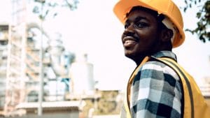 NEBOSH Environmental Management Certificate: Smiling engineer in hard hat at industrial plant.