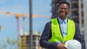 Occupational Health and Safety Coordinator. Smiling worker with hard hat and safety vest at construction site.