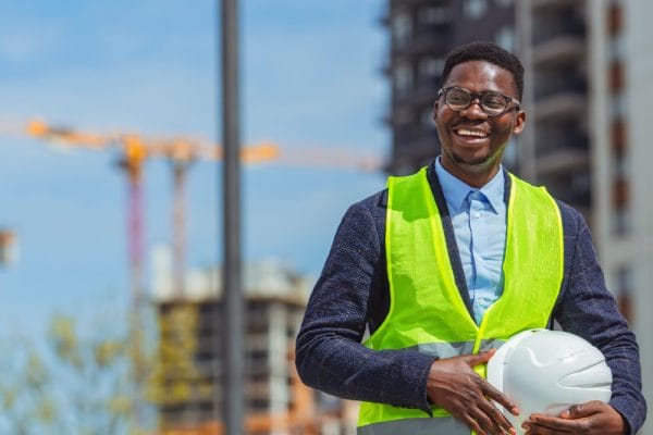 Occupational Health and Safety Coordinator. Smiling worker with hard hat and safety vest at construction site.