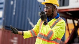 Occupational Health and Safety Representative. Worker with hard hat and safety vest using walkie-talkie at worksite.