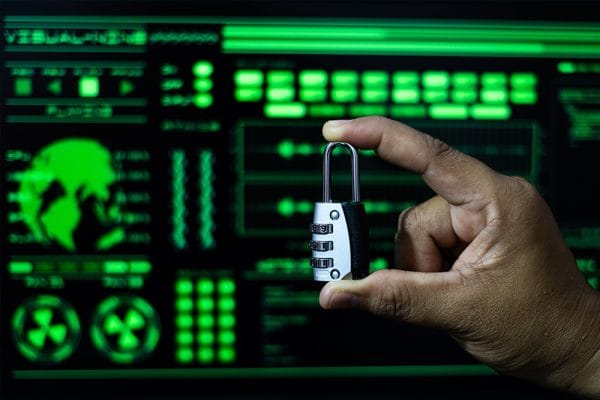DevSecOps introduction: Hand holding a padlock in front of a green computer screen. Security concept.
