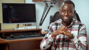 Java Novice to Javanista: Smiling programmer at desk with computer code. Software developer, coding, technology.