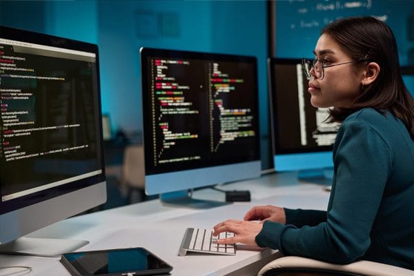 Woman coding PHP on multiple monitors. Learn PHP programming journey.
