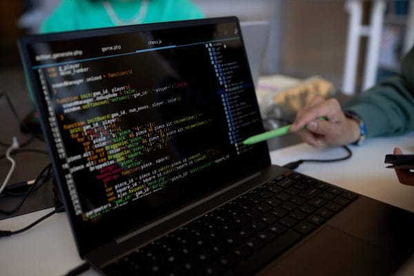 C++ programming: Laptop screen displays C++ code. A hand points to the code with a stylus. Focus on software development.