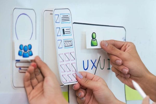 UI/UX design process. Hands arranging mobile app interface elements on a whiteboard. User experience planning.