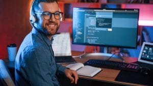 Front-End Engineer at desk with code on screen. Developer with headphones smiling. Software development job.