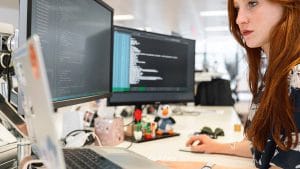 Microsoft Azure infrastructure design. Woman works on Azure solutions with dual monitors displaying code.