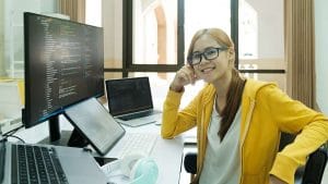 Microsoft Azure Administrator (AZ-104) candidate smiling at desk with multiple computers and coding on screen.