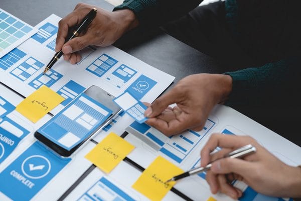 Android mobile development: App designers planning UI/UX with layouts and sticky notes.